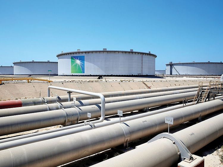 A large industrial oil pipeline stretches across a desert landscape toward a distant facility under a clear sky.