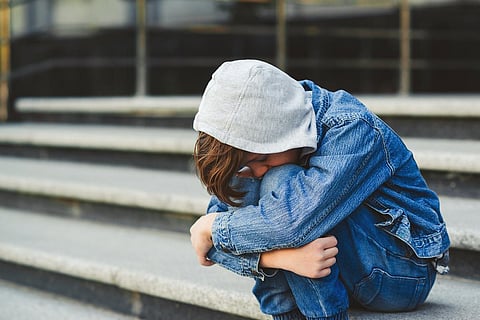 Concepto de acoso escolar. Niño sentado en la escalera, cubriéndose la cara. Triste joven colegial fuera de la escuela. Emociones negativas, depresión, estrés.