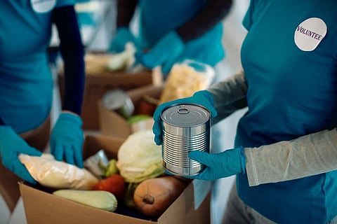 Unrecognizable people packing food in donation boxes while working as volunteers in charitable foundation. 