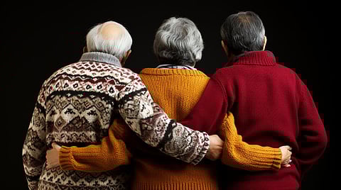 Rear view of three older people, two old men and in the middle an old woman, gray hair, winter knitted sweater, best friends or family and siblings, brother and sister, retirement age, backs, hugging each other, togetherness and looking into the darkness, death or dead or depression and worries and problems, fictional