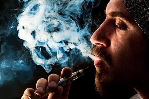 Iluminación dramática hombre barbudo fuma un cigarrillo electrónico 