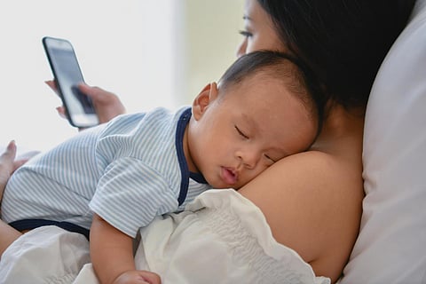 Concepto de recién nacido. Madre e hijo en una cama blanca. Mamá y bebé jugando en el dormitorio. La madre está jugando con el teléfono móvil en la cama.