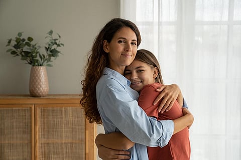 woman hugging teenage girl by a window