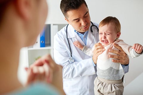 medicine, healthcare, pediatry and people concept - doctor or pediatrician holding sad crying baby girl on medical exam at clinic