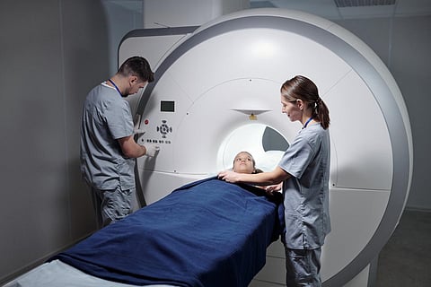 Young assistant preparing little girl for mri scan examination while doctor pushing buttons on panel of equipment
