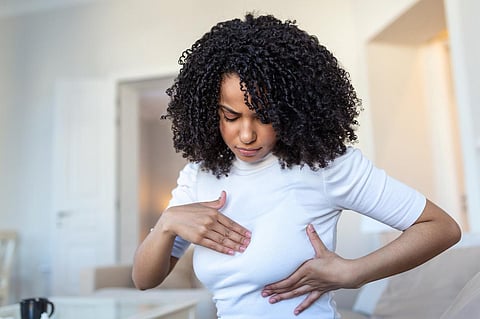 Joven mujer afroamericana palpando su seno por sí misma que se preocupa por el cáncer de mama. Concepto de atención médica y cáncer de mama