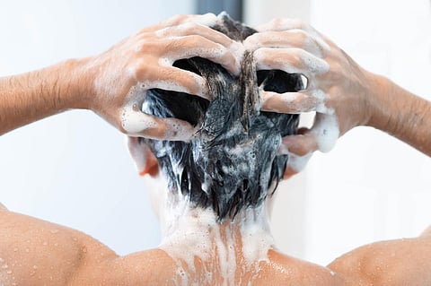 Closeup young man washing hair with with shampoo in the bathroom, health care concept, selective focus