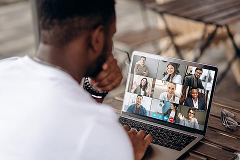 Video call. Online business meeting. Successful African American freelancer communicate by a video conference with his colleagues using a laptop while sitting in cafe in a summer terrace, they discussing about business affairs. On a laptop screen, participants of a video conference