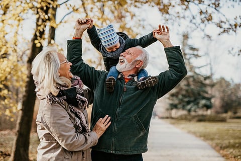 Happy good looking senior couple husband and wife walking and playing with their adorable grandson in public city park