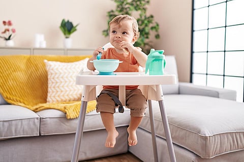 Adorable blond toddler sitting on highchair eating snack at home