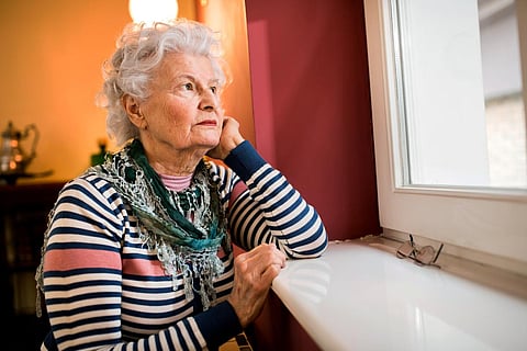 Sad alone senior woman looking through window at home, loneliness concept