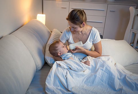 baby lying on mothers knees and drinking milk from bottle at night