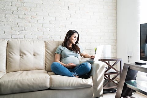 Full length of Caucasian pregnant female using laptop while sitting on sofa in living room
