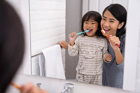 happy mom and kid brushing their teeth together in bathroom sink in the morning
