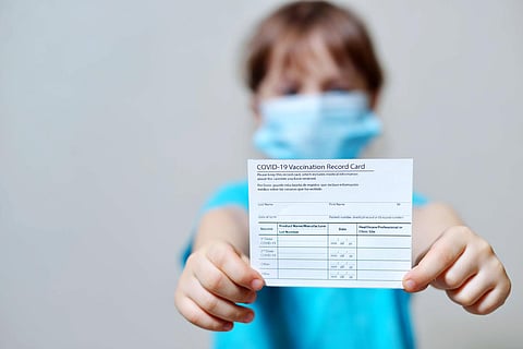 girl is holding a vaccination record card and corona virus vaccine vials. Passport of immunity to the coronavirus in the hands of a child. Health passport as proof of recovery from COVID-19