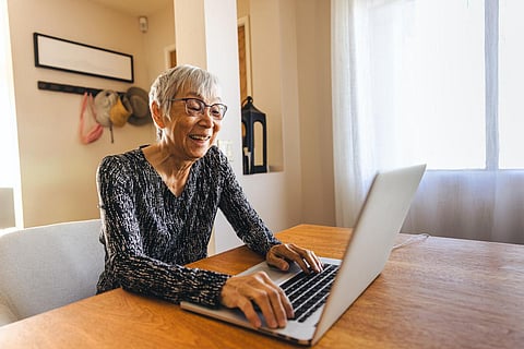 Happy senior woman using laptop on table in living room at home