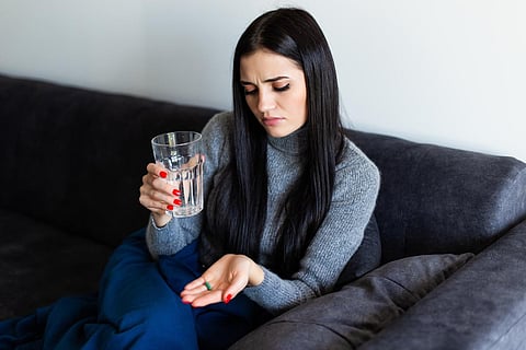 Pretty young woman holding a morning after pill and a glass of water at home
