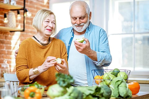 Portrait of a cheerful senior couple eating apples standing together with healthy food on the kitchen at home