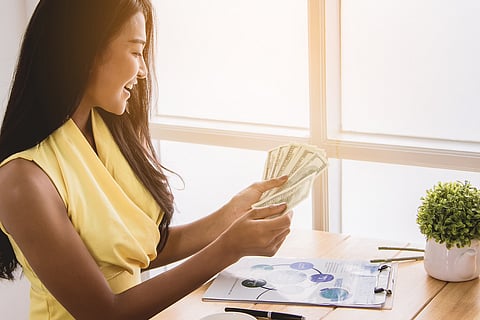 Woman in yellow blouse smiling while holding cash and money
