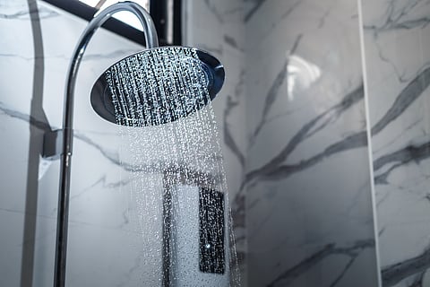 Shower head in bathroom with water drops flowing.