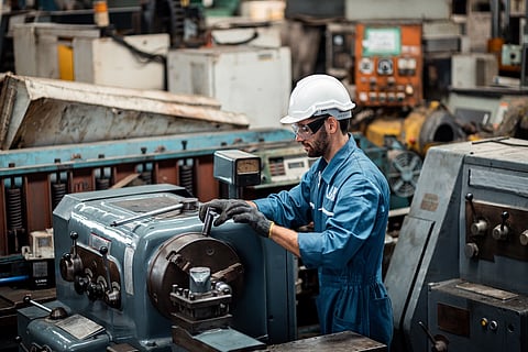 Men industrial engineer wearing a white helmet while standing in a heavy industrial factory behind. The Maintenance looking of working at industrial machinery and check security system setup in factor