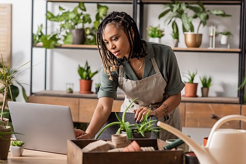 young african american florist using laptop near blurred flowerpots and watering can in flower shop