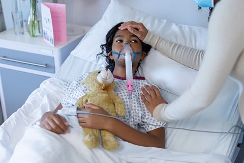 Mixed race mother in face mask touching sick daughter's head on oxygen ventilator in hospital