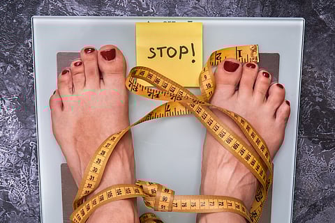 Stop Anorexia nervosa! Society perception, pressure about weight problem. Skinny female feet on a scale with yellow measuring tape. Loss weight social stigma. Body positive concept.