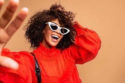 Portrait of beautiful young black woman taking selfie.Portrait of a pretty young afro american woman in retro style clothes smiling while standing and taking a selfie isolated over beige.