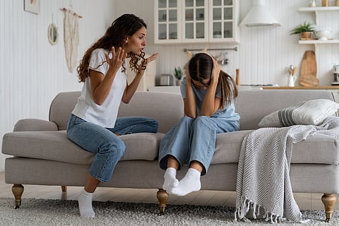 Madre enojada y loca tratando de disciplinar al niño, expresando frustración gritando a la hija adolescente sentada en el sofá tapándose los oídos con las manos. Efectos psicológicos de gritarles a los niños, abuso verbal