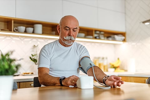 Portrait of a senior man with mustache measuring blood pressure at home.