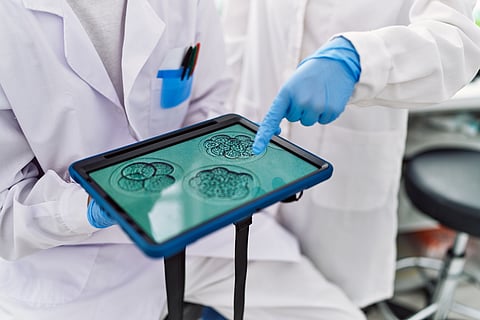 Pareja de hombre y mujer con uniforme de científico señalando con el dedo al panel táctil de imagen de embrión en el laboratorio
