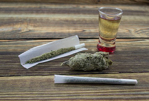 Joint, grinder, cannabis buds, alcohol shot and related items on a table.