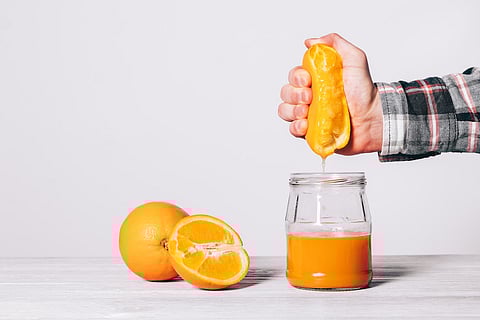 Hand squeezing juice from an orange in a glass jar