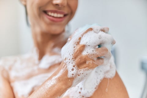 Young woman washing her body with bath loofah