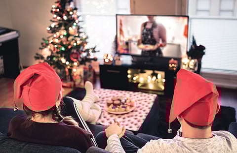 Couple watching tv on Christmas. Happy family holiday at home. Man and woman on couch relaxing with tree, decorations, lights, candles and television