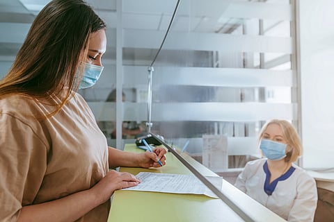 Female doctor or nurse explaining patient how to fill medical form at hospital reception