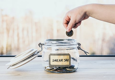Selective focus on child hand, put euro coin in swear jar. Every time child curses or swears it has to put money as punishment in jar for safe keeps.