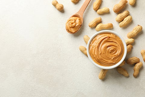 Spoon and bowl with peanut butter, and peanut on white background