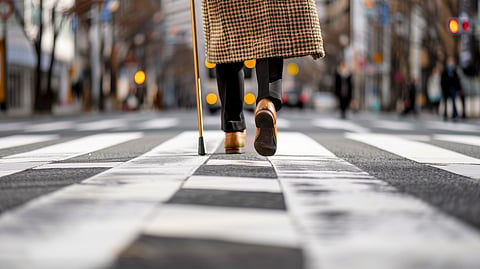 Elderly Person Crossing Street: A close-up view of an elderly person's legs as they cross a busy street, their cane tapping rhythmically on the pavement. 
