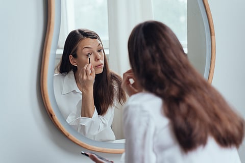 Tired brunette hispanic woman with loose hair white shirt looking at mirror holds brush, doing makeup, women morning routine. Beauty and self care. Mockup lady at morning