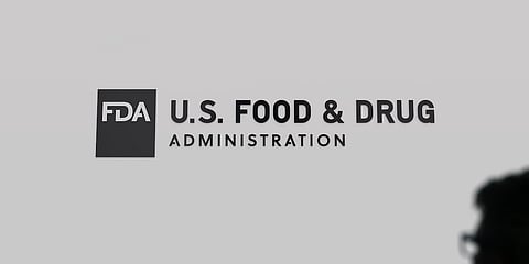 U.S. Food and Drug Administration, FDA's logo on a wall, on the foreground a blurry silhouette of a passer-by against the light.