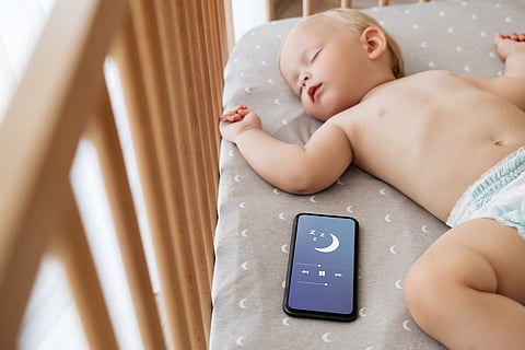 Baby sleeping in crib with sound app on phone
