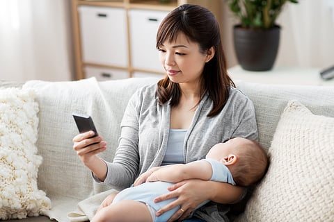 family, technology and motherhood concept - happy young asian mother with sleeping baby and smartphone at home
