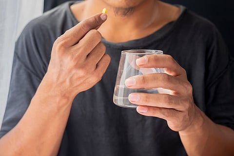 Asian man holding pills and a glass of water