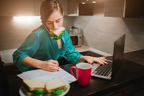 Busy woman eating, drinking coffee, talking on the phone, working on a laptop at the same time. Businesswoman doing multiple tasks.