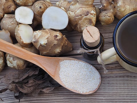 Fruits of the Jerusalem artichoke plant and natural syrup, drink in a mug and powder with inulin on wooden table, top view. Healthy helianthus tuberosus root vegetables and dietary supplements