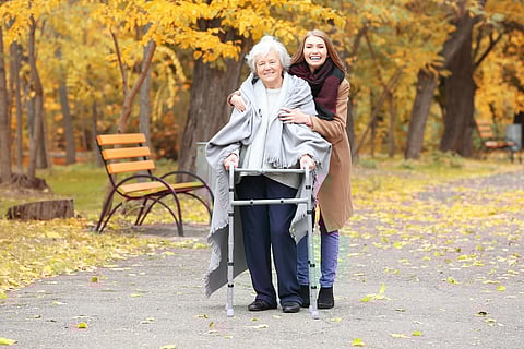 Senior woman with walking frame and young caregiver in park