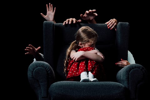 scared child sitting in armchair surrounded with human hands isolated on black