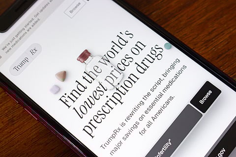 Angled close-up of smartphone showing TrumpRX website with medicine bottle and pills, discussing lower prescription drug prices in America today.